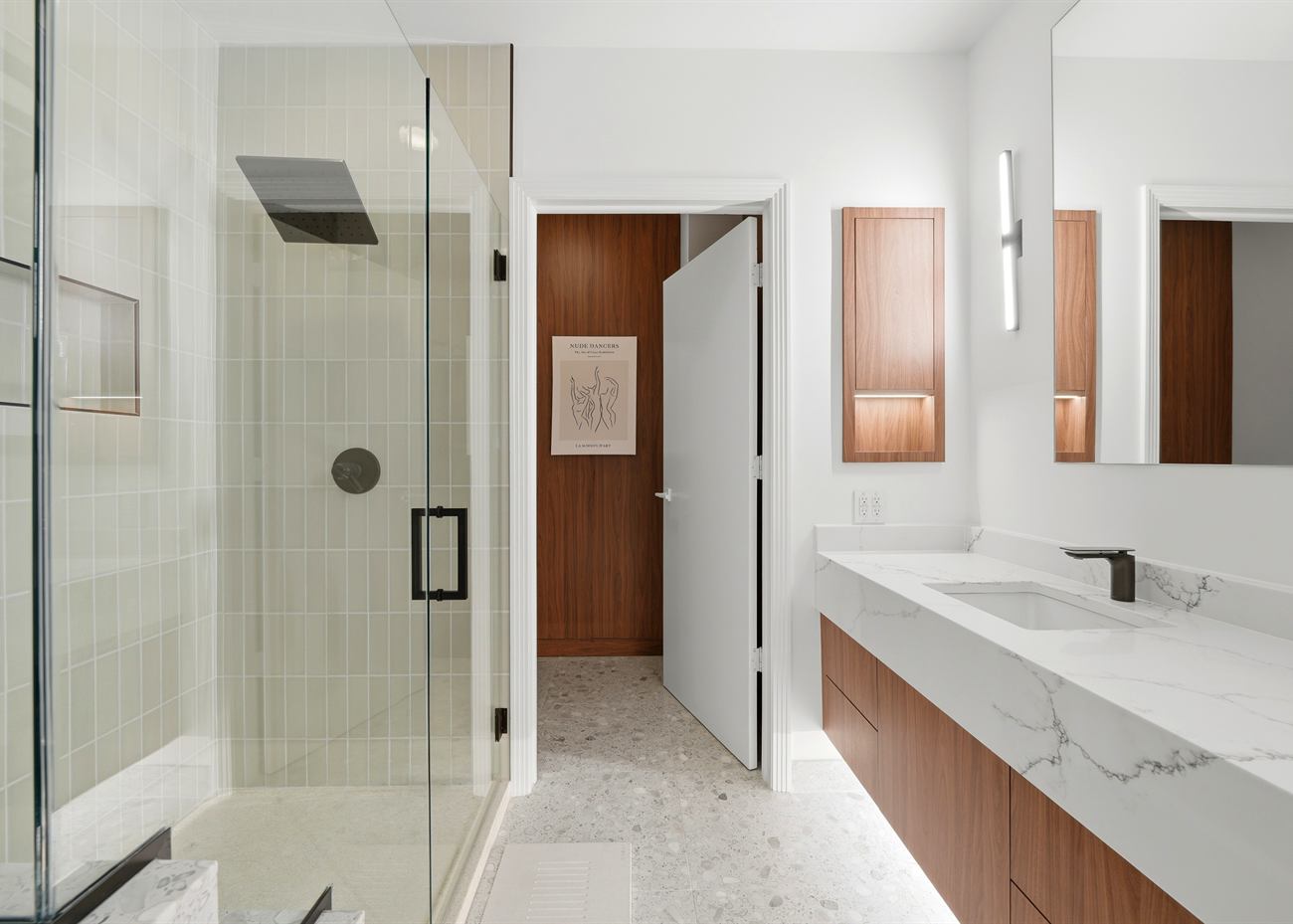 The same bathroom after renovation: stacked ceramic tile, frameless glass shower, walnut vanity with marble waterfall top