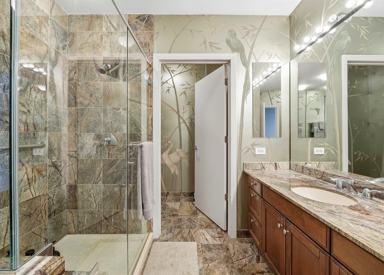 The primary bathroom before renovation: green marble shower and walls, dark timber vanity and granite top