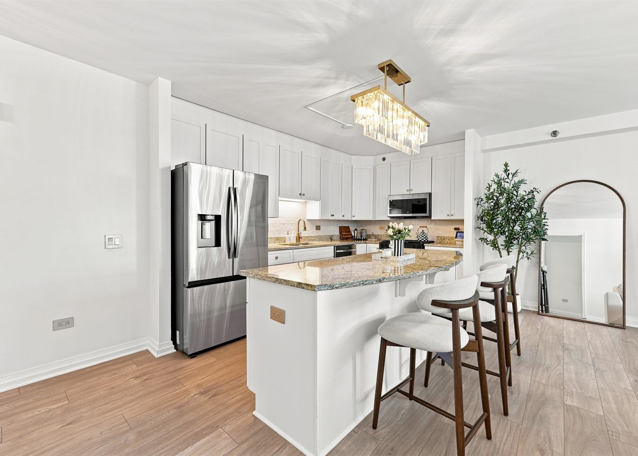 The same kitchen after renovation: white shaker cabinetry, brass linear pendant, new island and white oak floors