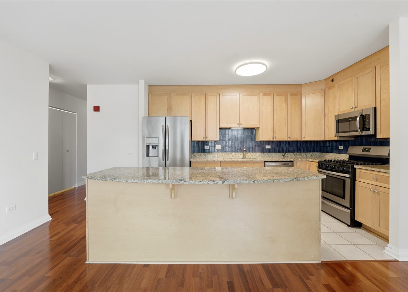The kitchen at 33 W Ontario before renovation: maple cabinetry, blue tile backsplash, granite island and tiled floor