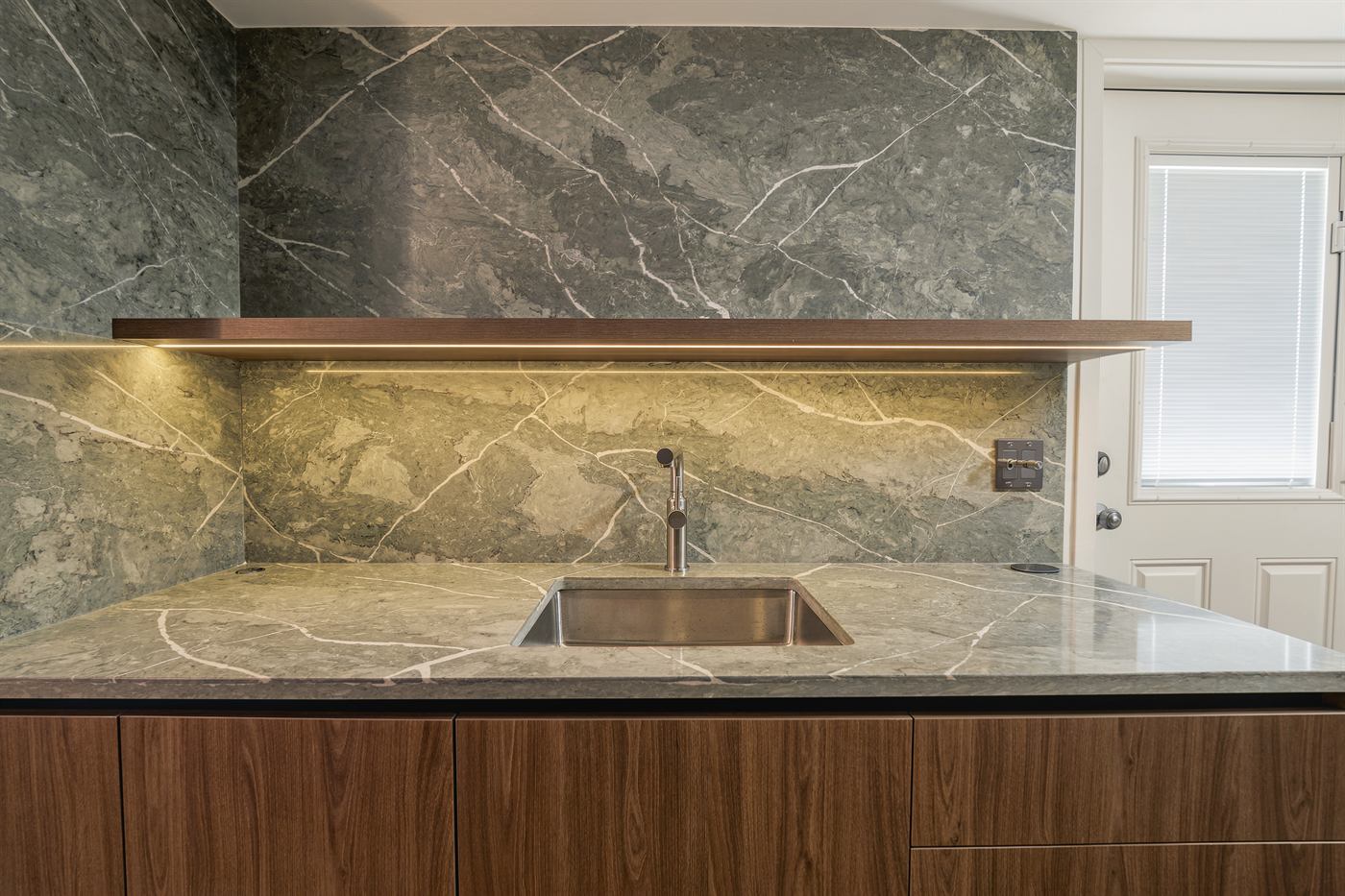 Green marble backsplash and counter with undermount sink and floating walnut shelf