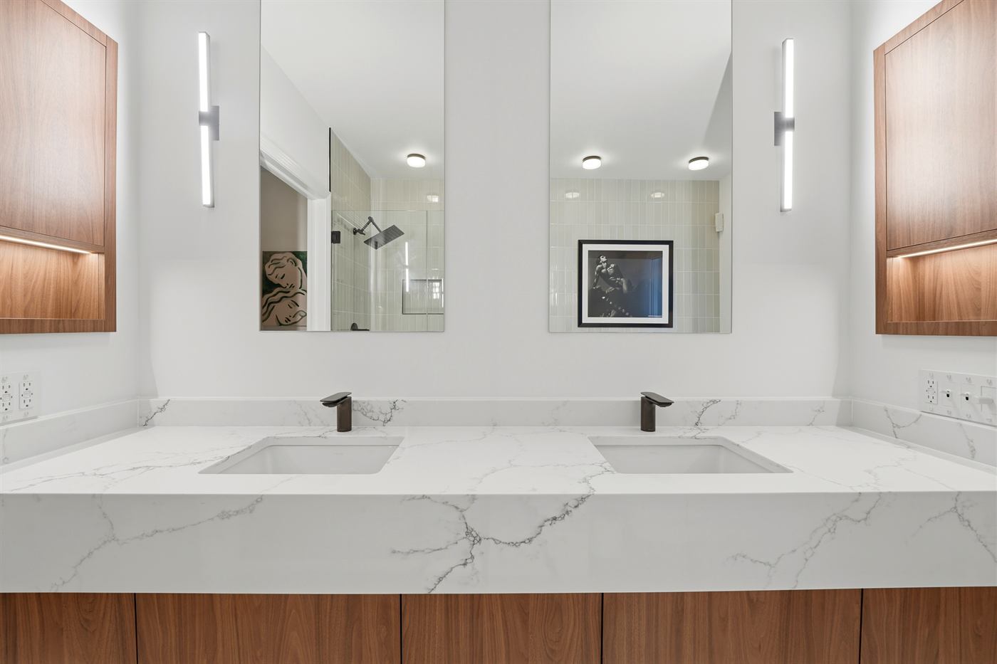 Double vanity with marble waterfall countertop, walnut cabinetry and backlit niches