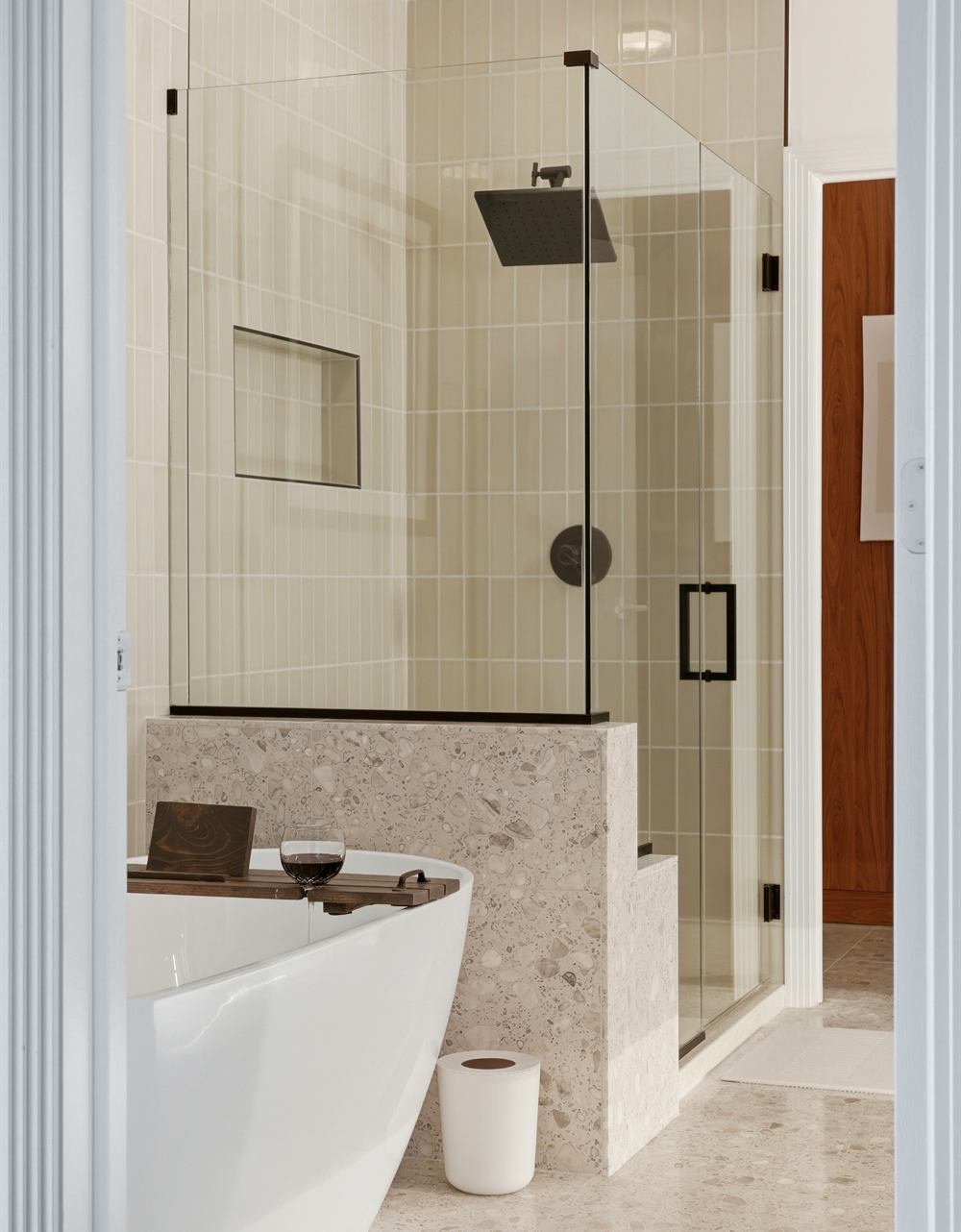 Freestanding soaking tub beside a glass-enclosed shower with stone bench