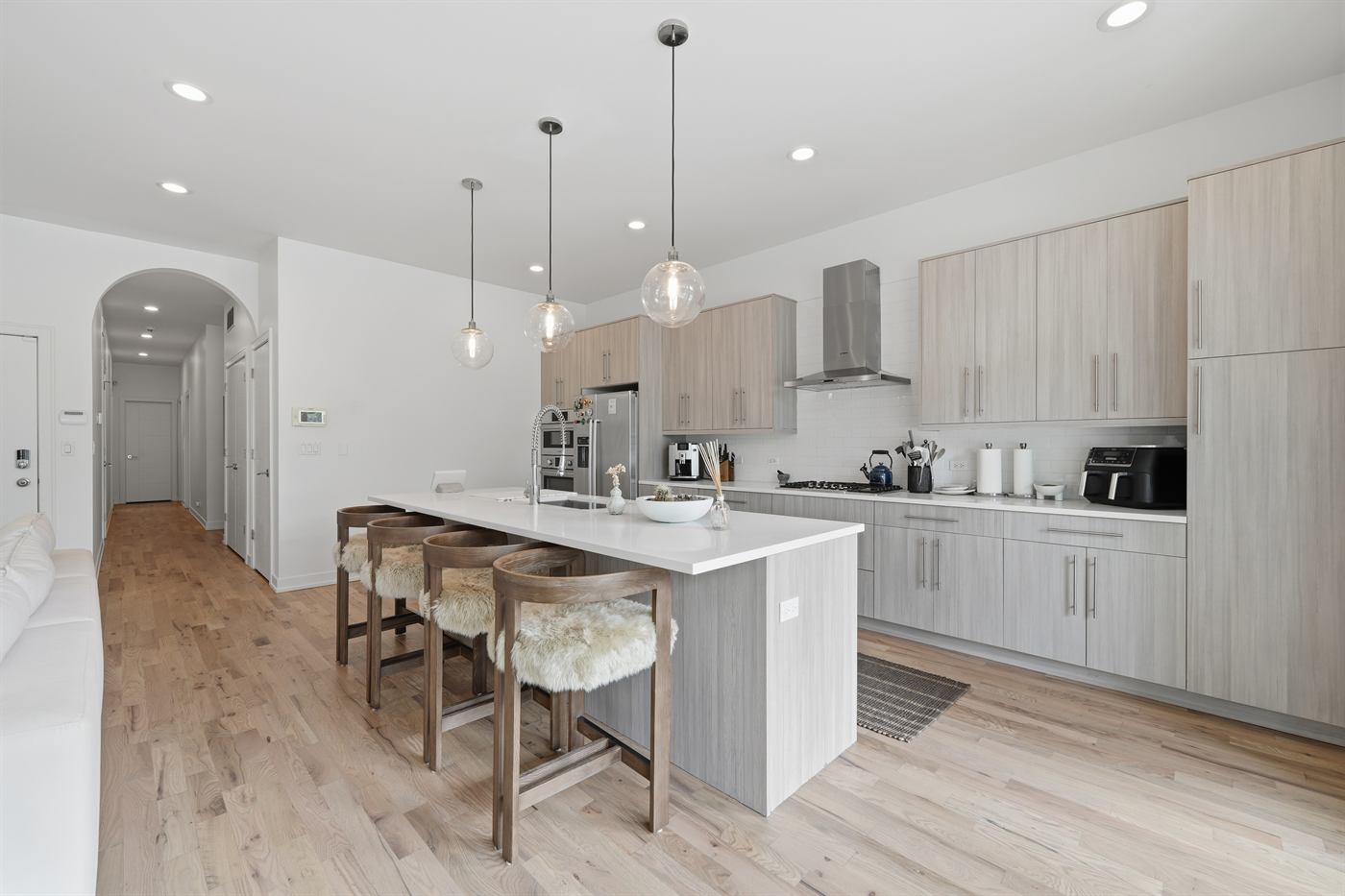 Kitchen run with pale timber cabinetry, stone counters and integrated hood